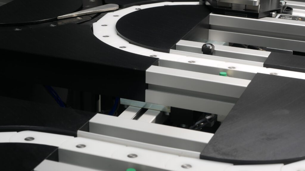 Detailaufnahme eines modularen Transfersystems mit Aluminiumprofilen, schwarzen und weißen Laufbahnelementen sowie einer Kurve zur Werkstückführung